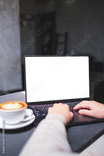 Vertical mockup image of a woman working and typing on laptop computer with blank white desktop screen in cafe