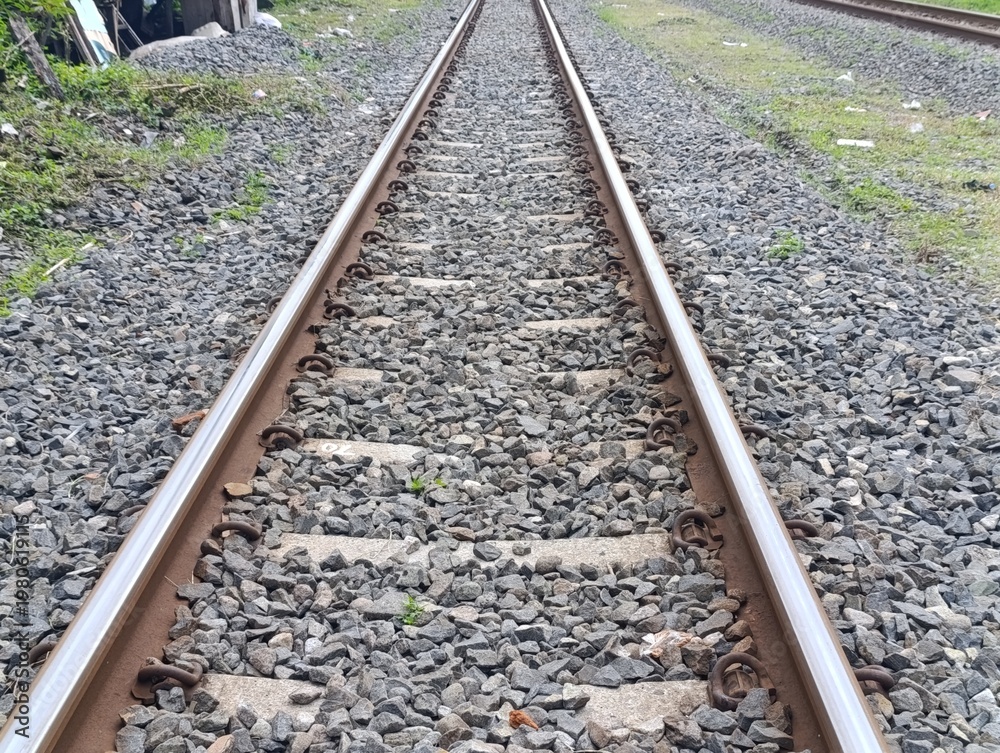 Fototapeta premium Railway tracks extending into the distance, gravel ballast, and green grass.