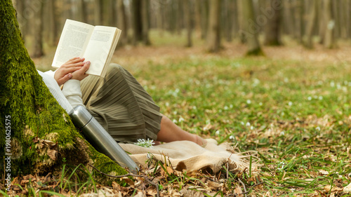 Woman reading a book while relaxing under a mossy tree in a spring forest