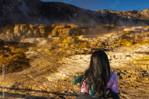 Fotografie A woman  gazes at the majestic, golden-hued travertine terraces of Mammoth Hot Springs in Yellowstone National Park