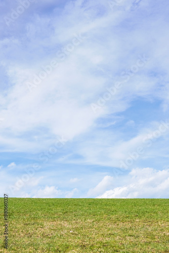 Wide view of blue sky with soft clouds above green field. Minimal natural background with large copy space and calm atmosphere.