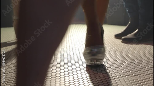  Elegant women's legs wearing high heels on a tiled floor with a moody cinematic atmosphere.
