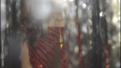 A woman in a shiny dress stands in silhouette against a curtain
