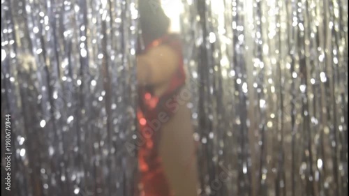 A woman in a shiny dress stands in silhouette against a curtain
