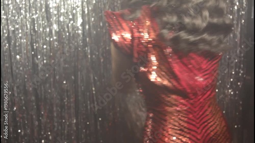 A woman in a shiny dress stands in silhouette against a curtain
