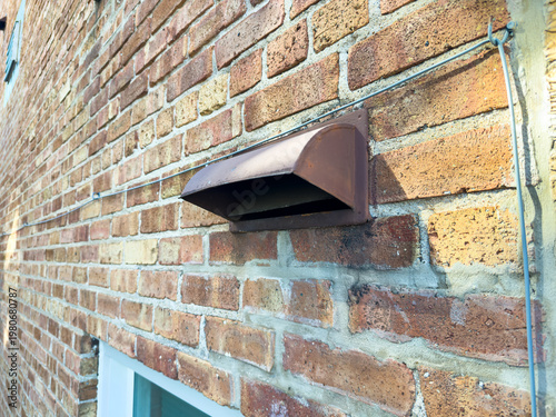 Copper vent installed on a brick wall in a residential setting during daytime hours