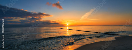 Panoramic sunrise over the Baltic Sea beach with wooden groynes and golden reflections on the water
