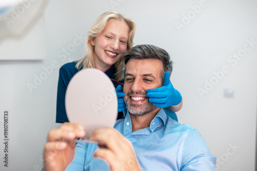 Billede på lærred Happy man looking in mirror after dental treatment with female dentist