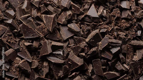 Broken crushed dark chocolate bits on background rotates, close up. Sweet food