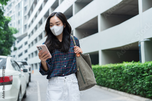 Obraz na plátně Young asian woman wearing face mask looking at phone