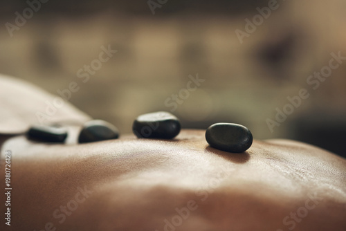 Photography Person, back and massage with hot rocks in spa for body treatment, pain relief or muscle relaxation