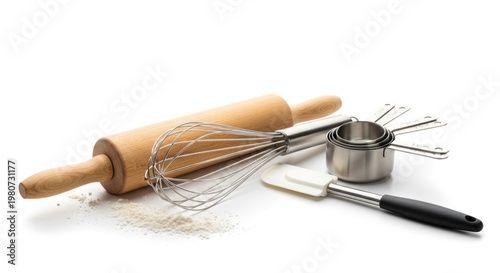 A wooden rolling pin, whisk, spatula, and measuring cups on a white surface with flour scattered around.