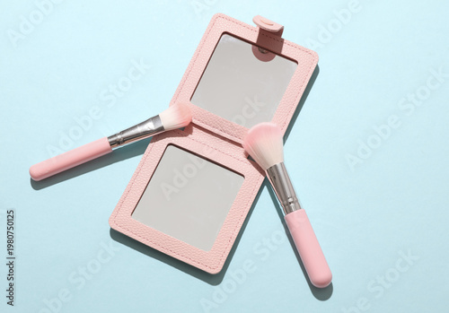 Pocket mirror and makeup brushes on a blue background. Beauty concept.