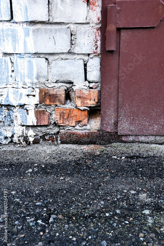 Weathered brick wall with rusty metal door and asphalt ground