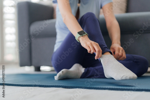 Adult Asian woman preparing for fitness activity adjusting sock on yoga mat at home comfortable sportswear for healthy lifestyle