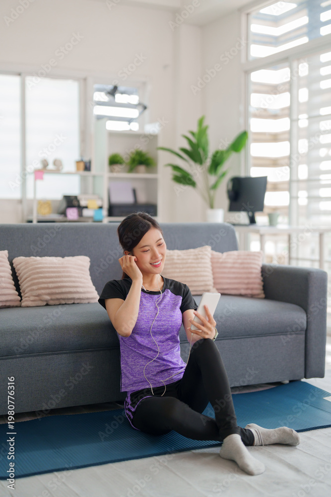 Obraz premium Asian adult woman sportswear enjoy listening music phone app sitting yoga mat home living room modern bright apartment fitness relaxation wellbeing wellness happy lifestyle