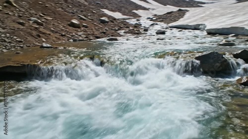 Spring meltwater rushing down a rocky mountain slope amidst snow patches