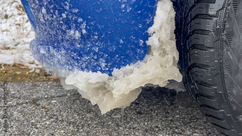 Konstfotografi Car wheel arch with ice buildup on snowy roadside pavement.