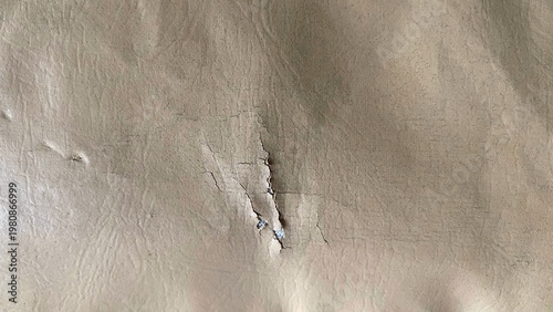 The texture of the cream-colored plaster wall with cracks and peeling parts in the middle, gives an old, damaged, and natural impression as a grunge background.