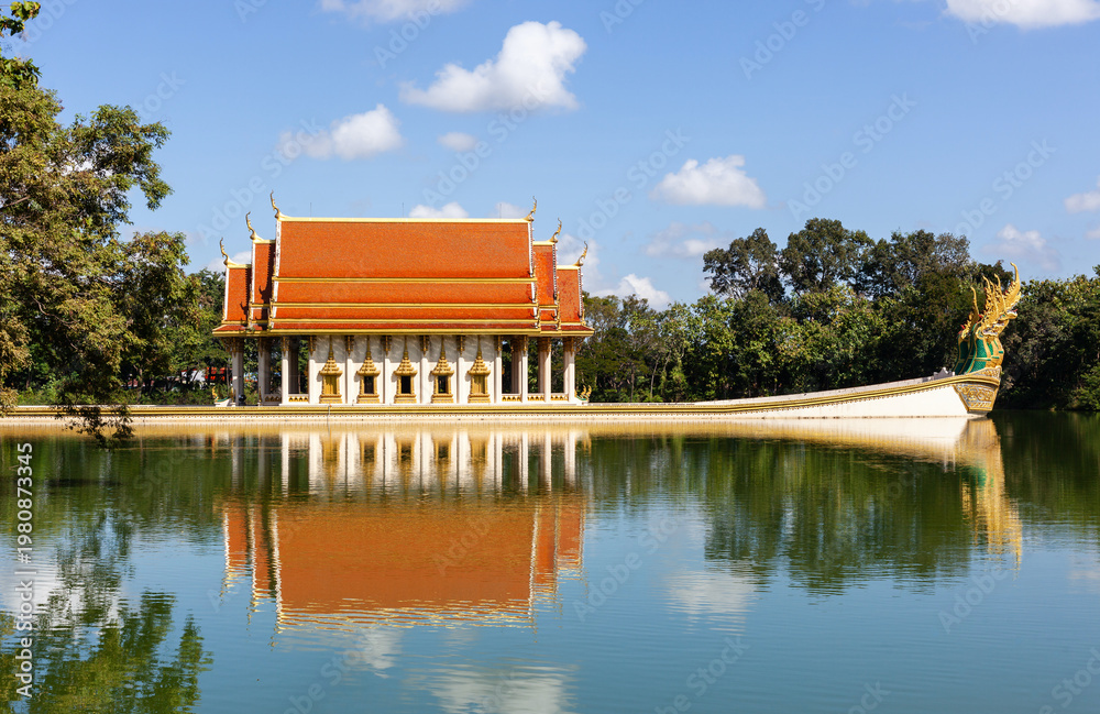 Fototapeta premium Wat Sa Prasan Suk temple reflection in lake. Traditional Thai architecture with orange roof. Located in Ubon Ratchathani, Thailand. Buddhist temple surrounded by nature.