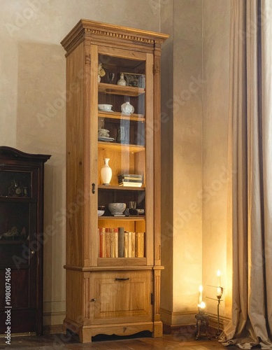 A tall, antique wooden display cabinet filled with decorative objects and books stands elegantly in a warmly lit interior, showcasing classic design and a sense of history.