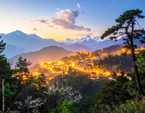A breathtaking view showcases a brightly lit hillside town nestled amongst majestic, snow-capped mountains at dusk.