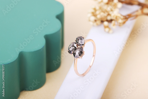 Fotografie Elegant rose gold ring featuring three unique salt and pepper diamonds on a white display stand with a soft teal and cream background