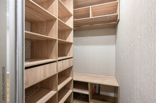 Fotografia light wood walk-in closet with open shelves, drawers, hanging rod, low bench, an