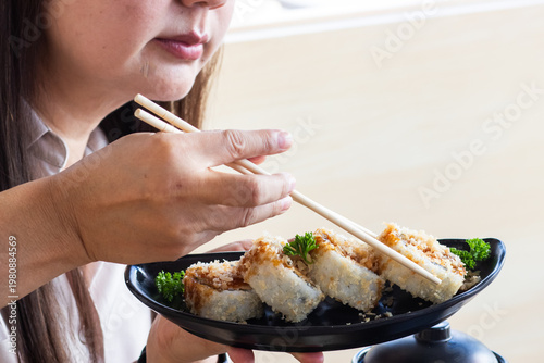 Close-up of a person using chopsticks to eat a crispy Salmon Tempura sushi roll, a vibrant and delicious Japanese lifestyle food photography.
