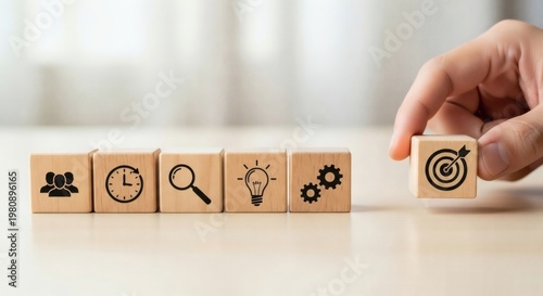 Business Strategy and Goal Setting Concept. Hand holding wooden cube with target icon near blocks with team time search idea and gear symbols, representing planning process and objective focus.
