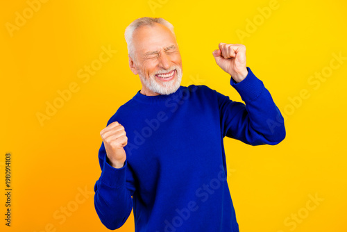 Obraz na płótnie Happy senior man celebrating victory in blue sweater against bright yellow backg