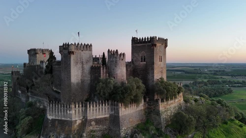 Aerial 4K drone view of the medieval Almodovar Castle in Cordoba, Spain at sunset. Ancient fortress on a hill during golden hour with scenic landscape.