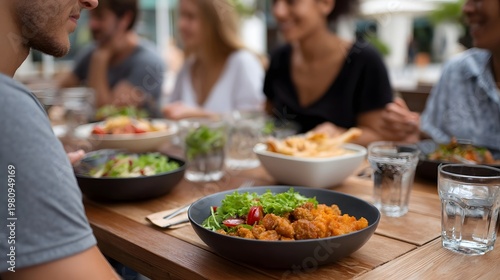 A group of friends gathered around a rustic wooden table sharing various dishes and appetizers in a bright casual setting
