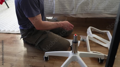 Adult male assembling office chair using hex key tool on wooden floor. Caucasian man hands screw chair lifting mechanism. Assembling office chair.