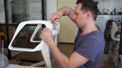Adult male assembling office chair using hex key tool on wooden floor. Caucasian man hands screw chair lifting mechanism. Assembling office chair.