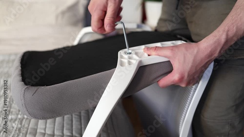 Adult male assembling office chair using hex key tool on wooden floor. Caucasian man hands screw chair lifting mechanism. Assembling office chair.
