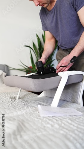 Adult male assembling office chair using hex key tool on wooden floor. Caucasian man hands screw chair lifting mechanism. Assembling office chair.