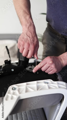 Adult male assembling office chair using hex key tool on wooden floor. Caucasian man hands screw chair lifting mechanism. Assembling office chair.