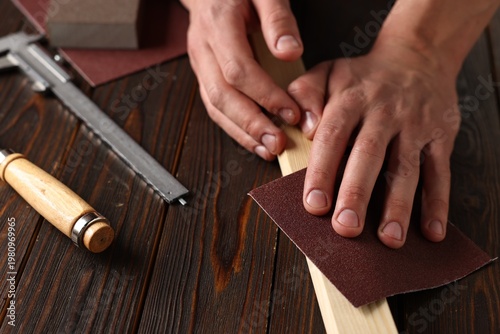 Foto Man polishing wooden plank with sandpaper at table, closeup