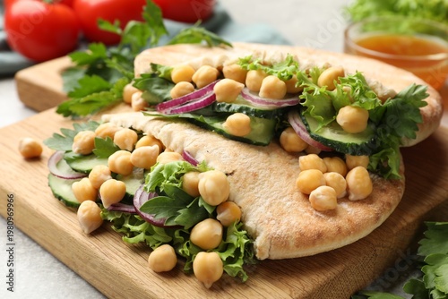 Pieces of pita bread with chickpeas and vegetables served on light grey table, closeup