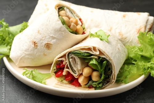 Pieces of wrap with chickpeas and vegetables served on black table, closeup