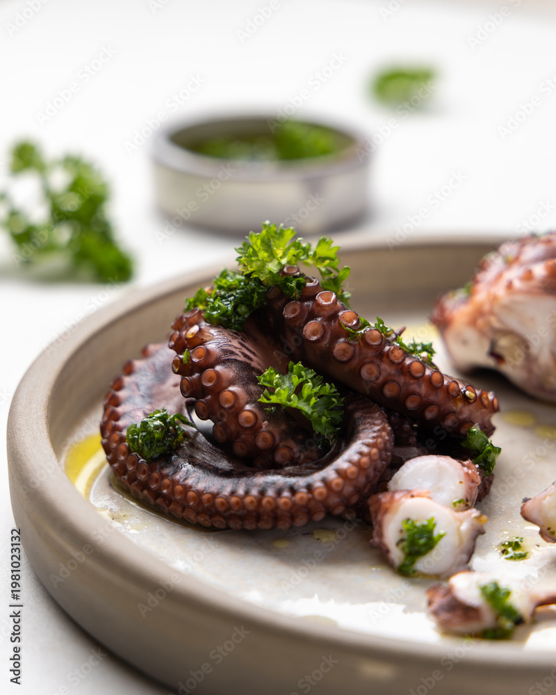 Fototapeta premium Boiled octopus tentacles and sliced pieces on ceramic plate close up. Olive oil and parsley dressing
