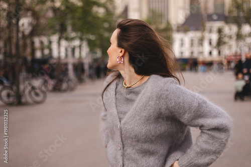 Obraz na plátne Profile view of a young woman looking away at a European city square, wearing a
