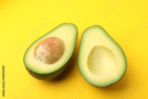 Halves of fresh avocado on yellow background, closeup