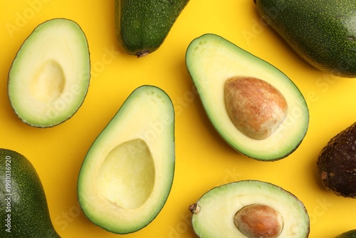 Whole and cut fresh avocados on yellow background, flat lay