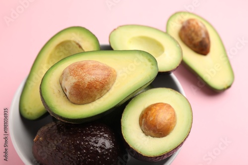 Whole and cut fresh avocados on pink background, closeup