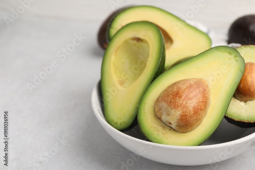 Whole and cut fresh avocados on white table, closeup. Space for text