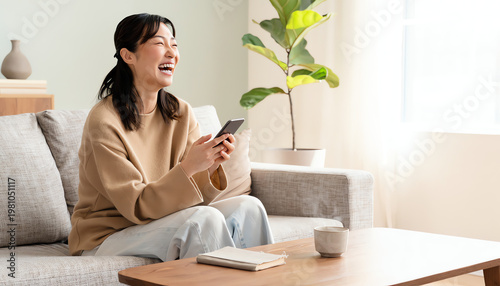 A joyful woman sitting on a sofa, laughing while holding a smartphone in a bright, cozy living room.
