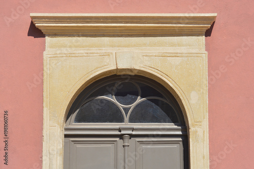 Detail of a traditional arched stone portal and lintel above a grey wooden door set into a salmon pink building facade