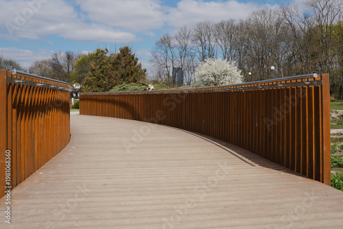 Modern curved wooden bridge in a city park under a blue sky with white clouds